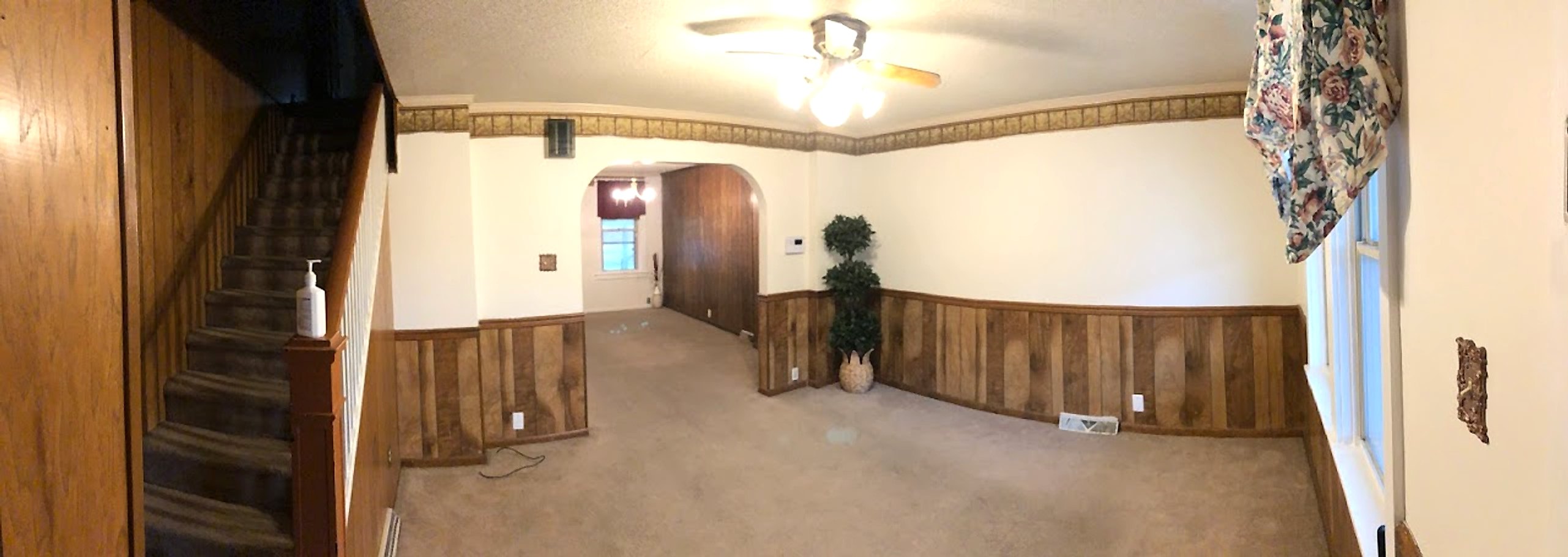 Living room before painting, with dark wood paneling, a wallpaper border and carpet