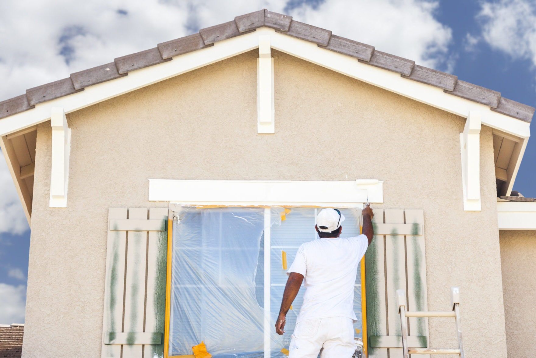 Painter painting the exterior trim and shutters of a house